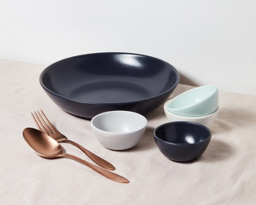 low wide navy bowl sitting behind 4 small multi-colored bowls and large copper spoon and fork