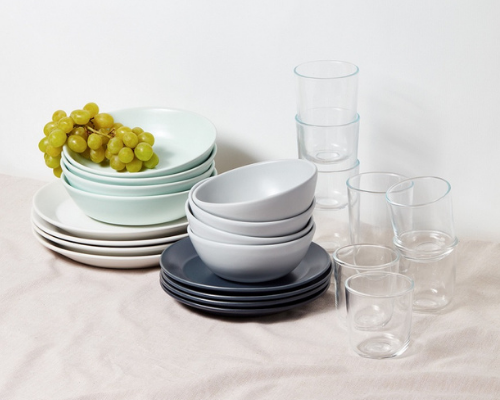 stack of 4 mint colored large bowls sitting on stack of 4 white dinner plates next to stack of grey bowls sitting on 4 smaller navy plates and stacks of short and tall clear drinking glasses