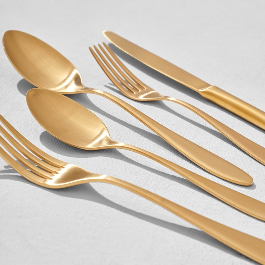 Close up of satin gold knife with satin gold spoons and forks