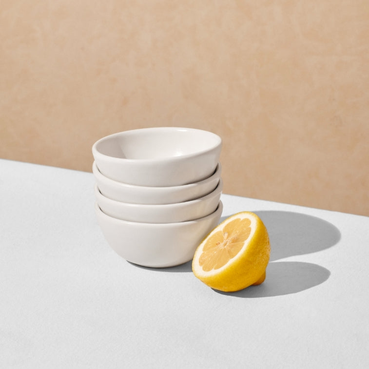 Stack of four off white mini bowls next to lemon half