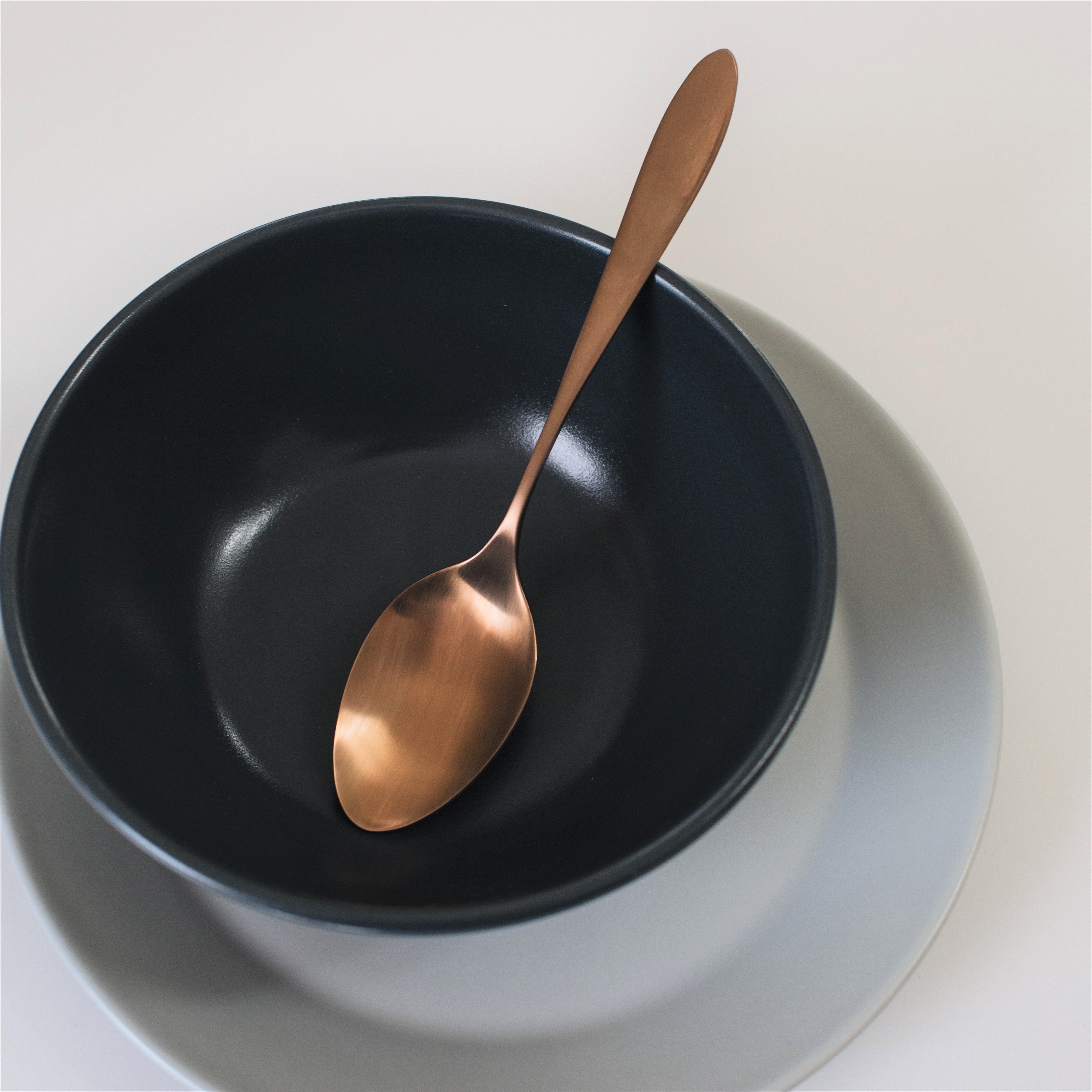 Satin copper breakfast spoon resting in charcoal navy bowl