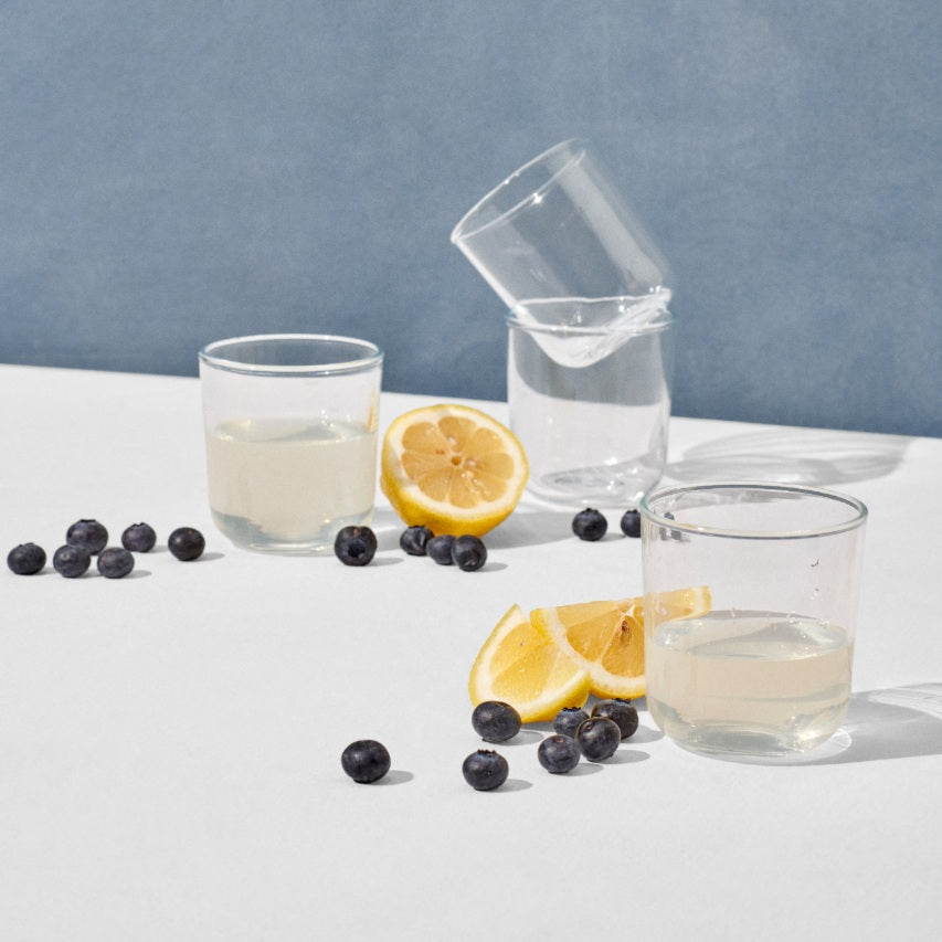 Four short drinking glasses surrounded by blueberries and lemon slices