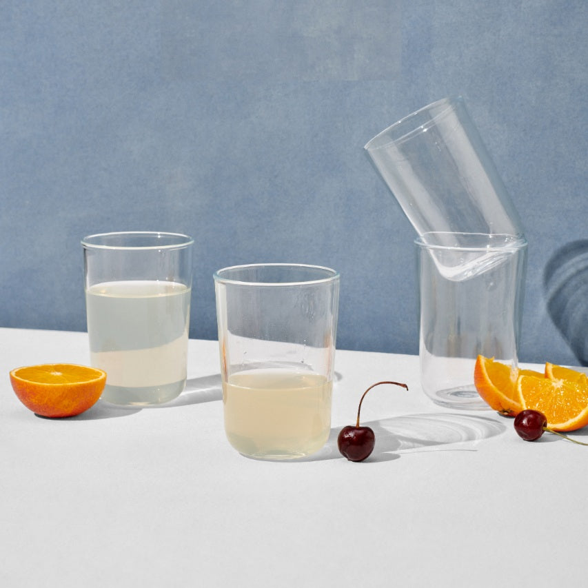 Four tall drinking glasses surrounded by cherries and orange slices