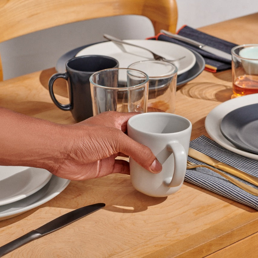 Hand placing grey mug on table next to plates and glasses